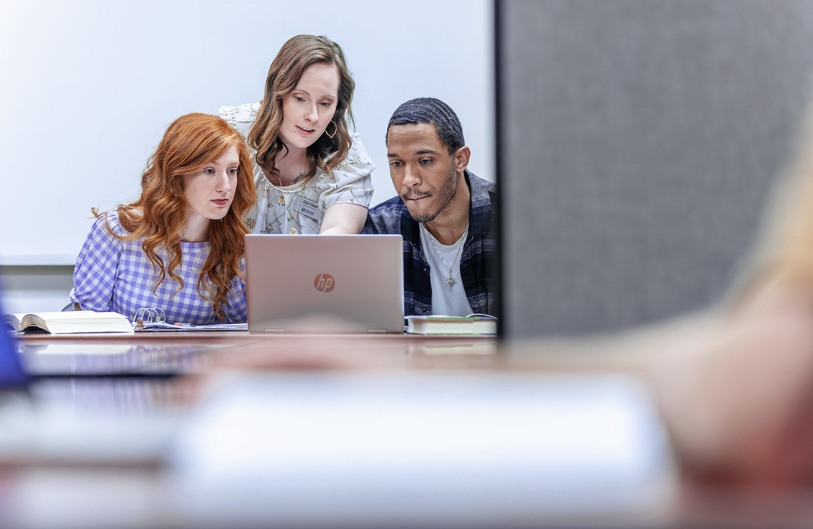 instructor behind students pointing at computer