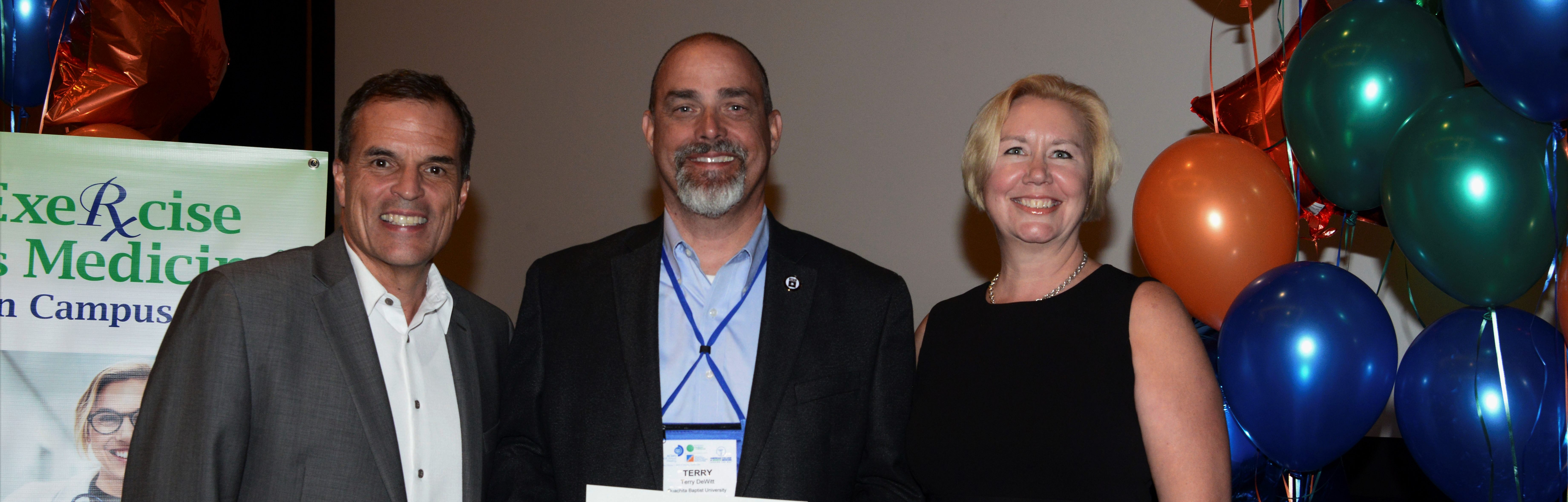 Dr. Terry DeWitt (center) accepts Ouachita’s first Gold Status credential for its Exercise is Medicine (EIM) program during the American College of Sports Medicine’s (ACSM) annual meeting in Orlando this summer. Bob Sallis, past-president of ACSM and EIM founder, and Renee Jeffries Heil, current EIM Committee chair, presented the award.