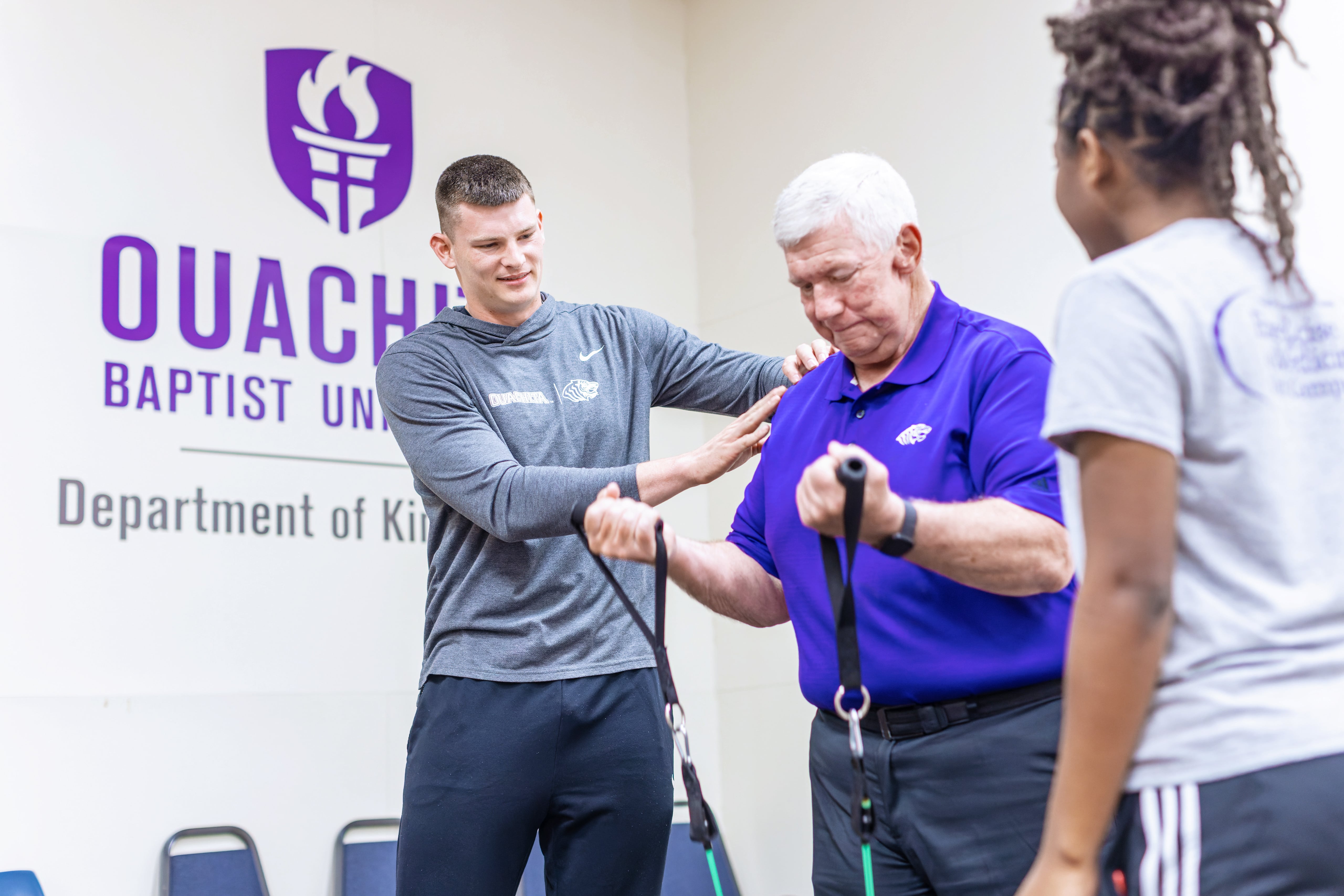 Exercise science students assist male as he uses exercise equipment